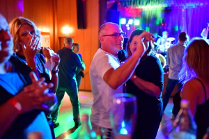 Festsaal mit farbigem Licht: Tanzende Personen winken und klatschen, während im Hintergrund Musik und Deko die Stimmung tragen.
