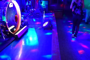 Bühne mit Scheinwerfern und Ringlicht; farbiges Licht beleuchtet Kabel, Technik und Boden, wirkt als Hintergrund für eine Feier/Show.