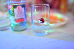 Zwei transparente Gläser auf einem Tisch, jeweils mit Symbolaufkleber, im Hintergrund unscharfe Partydekoration und farbiges Licht.