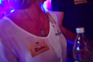 Nahaufnahme eines Teilnehmers mit Halskette bei Eventbeleuchtung in Blau und Magenta; Stimmung und Anlass werden inszeniert.