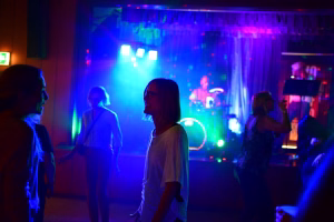 Feierabend-Bühne mit farbigen Lichtstrahlen, eine Sängerin im Vordergrund, dahinter Musiker und Publikum beim Live-Konzert.