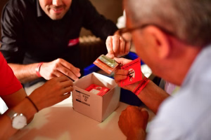 Personen öffnen eine Versandkiste und reichen ein Paket mit eingeloggten Karten zur Verteilung im Rahmen einer Feier.