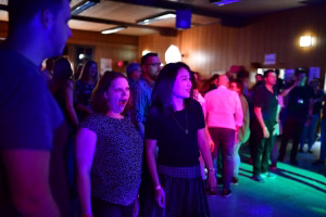 Personengruppe in festlichem Saal, beleuchtet von bunten Bühnenlichtern; Publikum steht seitlich und schaut nach vorn, Stimmung bei Veranstaltung.