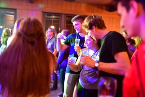 Menschen stehen in einer festlich beleuchteten Halle und trinken mit Strohhalmen, während sie miteinander ins Gespräch kommen.