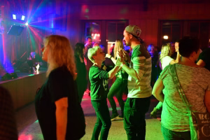 Feierabend auf einer Tanzfläche: mehrere Menschen in Party-Kleidung, beleuchtet von bunten Lichtern und Scheinwerfern, beim Tanzen und Zusammensein.