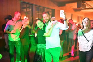 Feiernde Menschen tanzen in geselligem Ambiente, heben die Hände und lächeln in farbigem Licht; dient der Darstellung von Party-Stimmung.