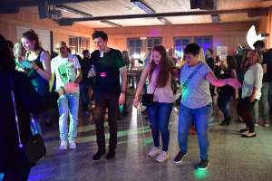 Festsaal mit beleuchteter Tanzfläche: mehrere Personen feiern und bewegen sich zur Musik, im Hintergrund weitere Gäste und ein Bühnenlicht.