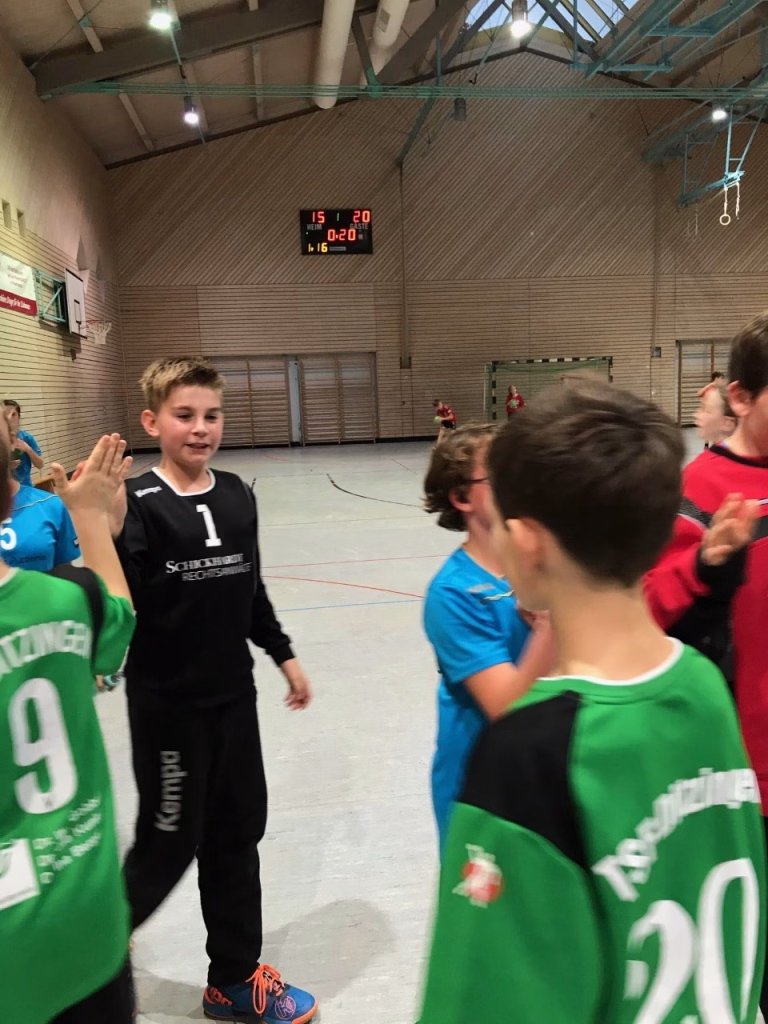 Jungen und Mädchen im Hallensportbereich winken und jubeln nach dem Spiel; Anzeigetafel im Hintergrund zeigt laufende Punktzahl.