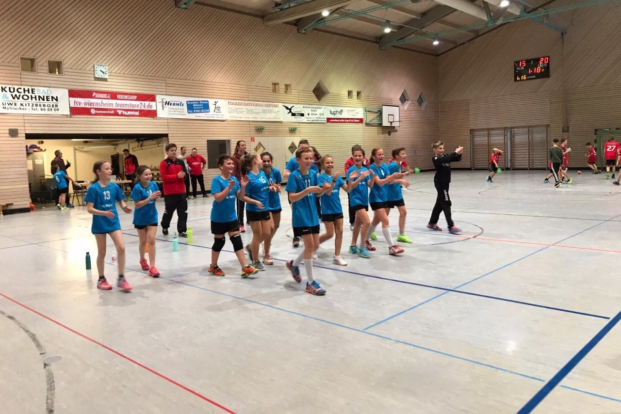 Handballteam in Hallensporthalle jubelt geschlossen nach dem Spiel, Kinder und Jugendliche in blauen Trikots und gestikulierender Freude.