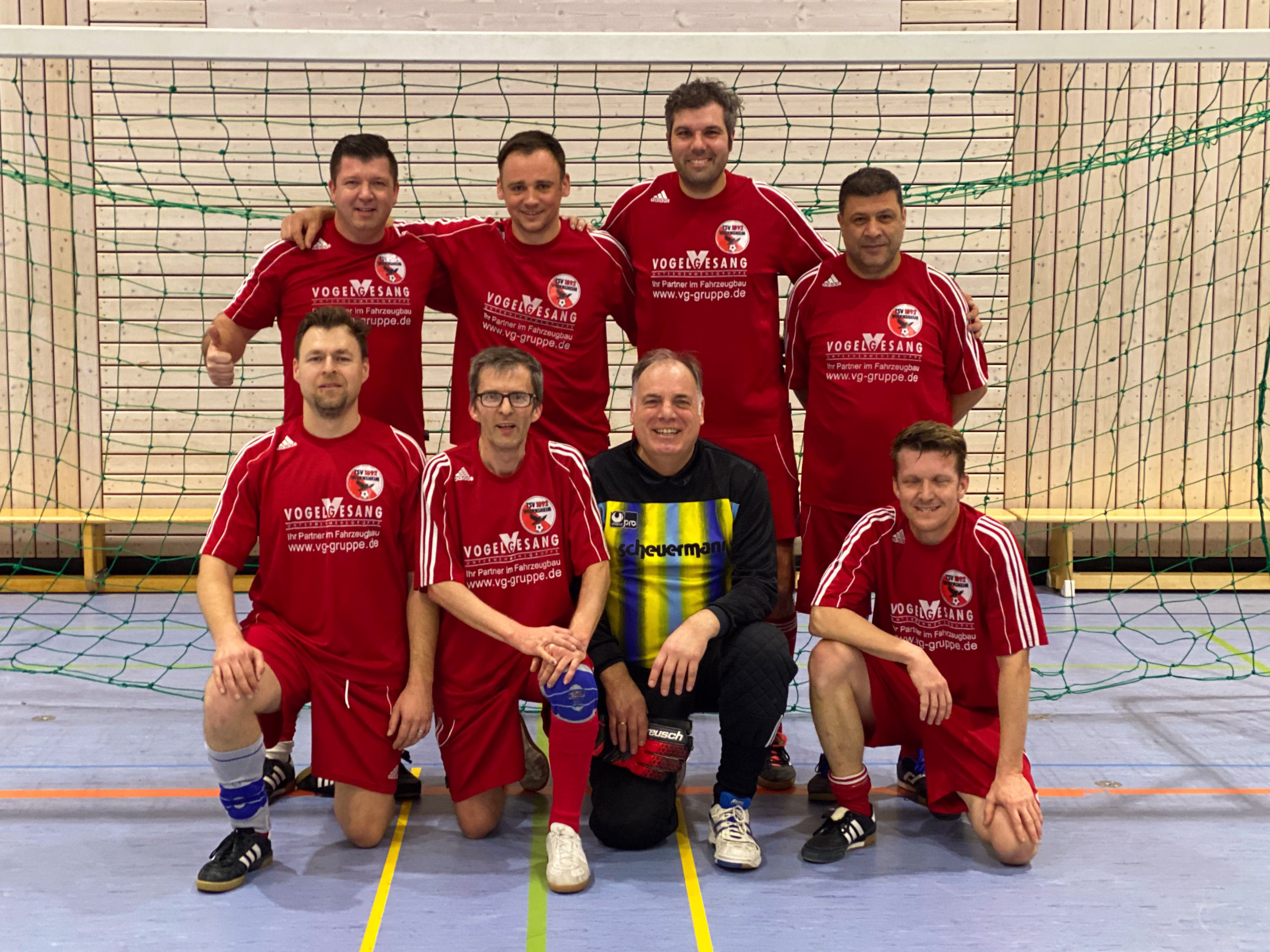 Mannschaftsgruppe im Hallenfußball: acht Spieler in roten Trikots posieren vor dem Tor und demonstrieren Teamzugehörigkeit.
