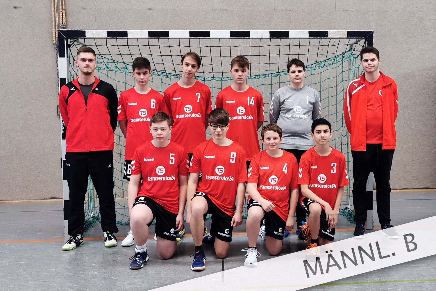 Handballmannschaft in Trainingsoutfits vor einem Tor, posierend für ein Teamfoto; Vorderreihe sitzt, Hinterreihe steht.