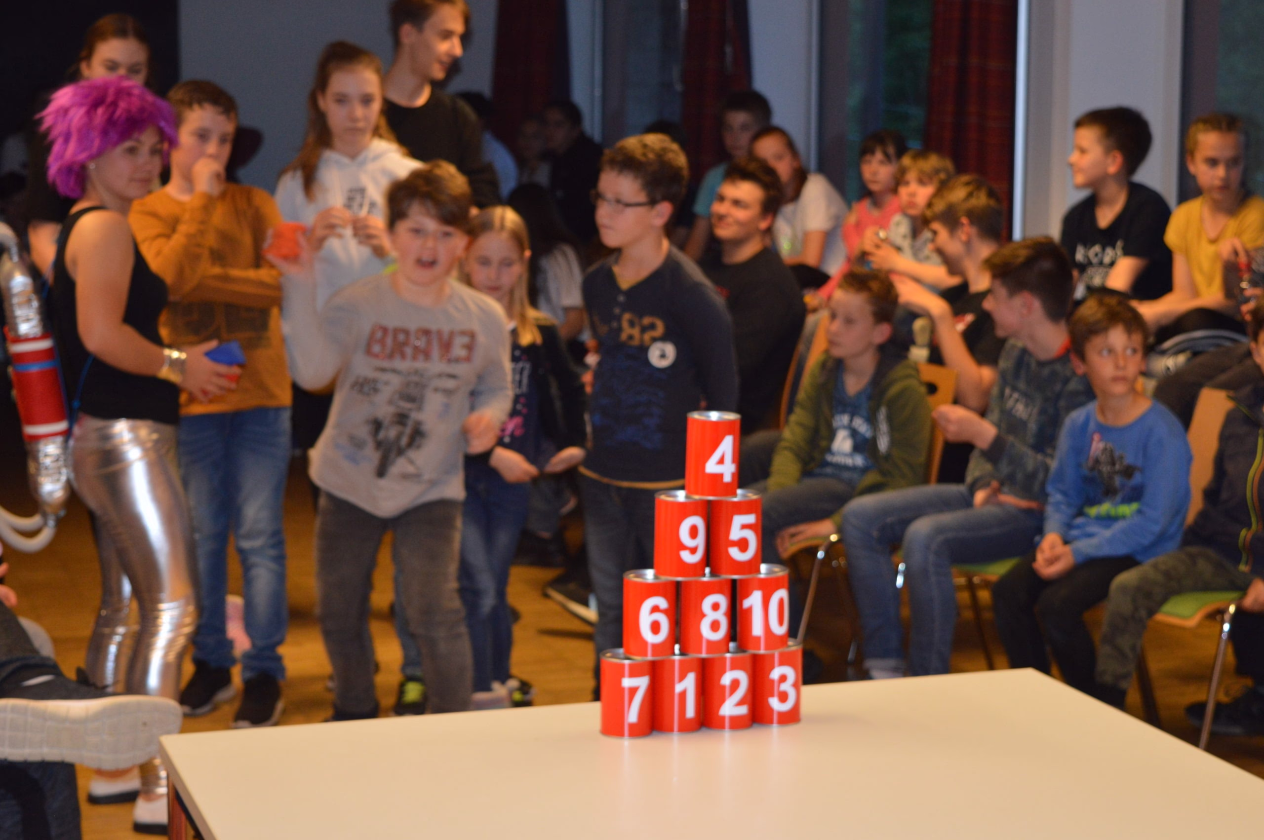 Kinder stehen beim Spiel um einen Stapel roter Zahlenbecher (1 bis 10) und verfolgen aufmerksam die nächste Runde.