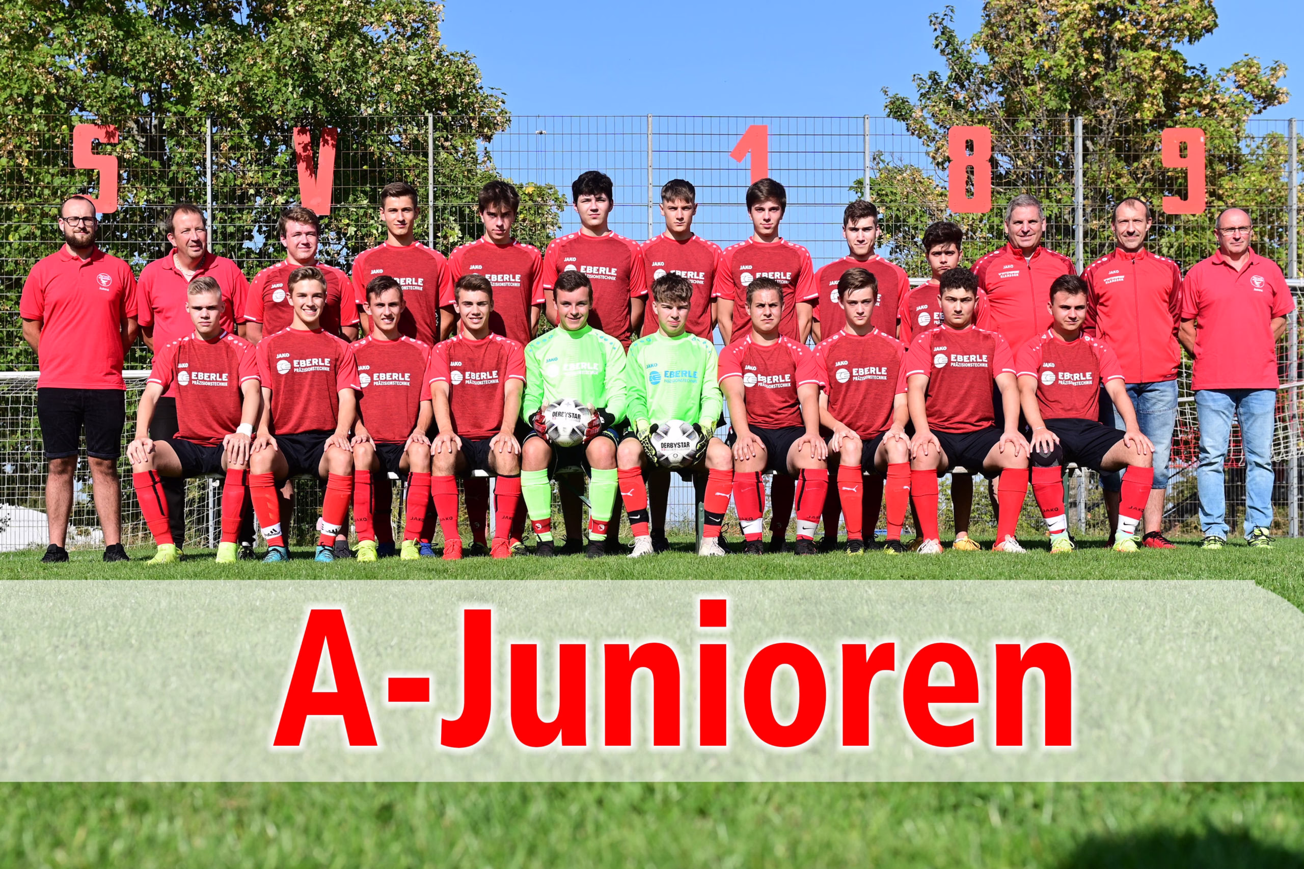 Mannschaftsfoto einer Fußball-Jugendmannschaft im Trikot vor Zaun und Tor, darüber große Ziffern „5 V 1 8 9“ und Schrift „A-Junioren“.