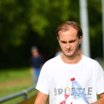 Sportlicher Mann im Freien, Blick nach unten, hält eine transparente Wasserflasche mit rotem Verschluss in der Hand.