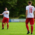 Zwei Fußballspieler auf einem Rasenplatz, einer steht von hinten im Vordergrund mit Rückennummer, im Hintergrund spielt er mit Blick zum Spiel.