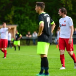 Zwei Fußballspieler auf dem Trainingsplatz, einer im weißen Trikot dreht sich beobachtend zur Seite, der andere im Vordergrund läuft.