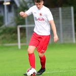 Fußballspieler im Spiel: läuft am Ball vorbei, ein Bein setzt zum Dribbling an, draußen auf dem Rasen vor dem Tor.