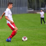 Fußballspieler im Laufduell auf dem Rasen, blickt seitlich und spielt den Ball kontrolliert Richtung Mitspieler.