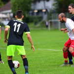 Fußballspieler beim Spiel auf dem Rasen, einer kniet, ein anderer läuft mit Ball an und bereitet eine Aktion im Abseitsraum vor.
