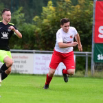 Zwei Fußballspieler im Sprint gegeneinander, ein Ball im Vordergrund; während eines Spiels auf dem Rasen.
