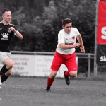 Zwei Fußballspieler sprinten im Spiel, während ein Ball im Vordergrund über den Rasen rollt; Aufnahme eines Spiels der laufenden Aktion.