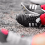 Nahaufnahme eines schwarzen Turnschuhs am Boden, mit rotem Strickschuhbein in der Hand bei sportlicher Vorbereitung/Arbeit.