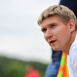 Nahaufnahme eines Jungen mit kurzen blondem Haar im Sportoutfit, Blick nach links; unscharfer Hintergrund zur Kontextgebung.