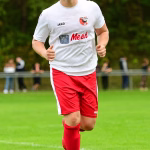 Fußballspieler im weißen Trikot und roten Hosen läuft im Stadion und hält die Arme zum Beschleunigen vor dem Spiel bereit.