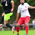 Zwei Fußballspieler kämpfen um den Ball im Laufduell, einer schießt/greift an, auf dem Rasen vor unscharfem Hintergrund.