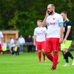 Fußballspieler im weißen Trikot mit erhobener Hand, der ein Spielgeschehen während eines Matches an der Seitenlinie anzeigt.