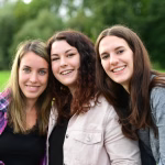 Drei Personen posieren dicht nebeneinander im Grünen; unscharfer Hintergrund, Lächeln und freundliche Gesichter für ein Porträt.